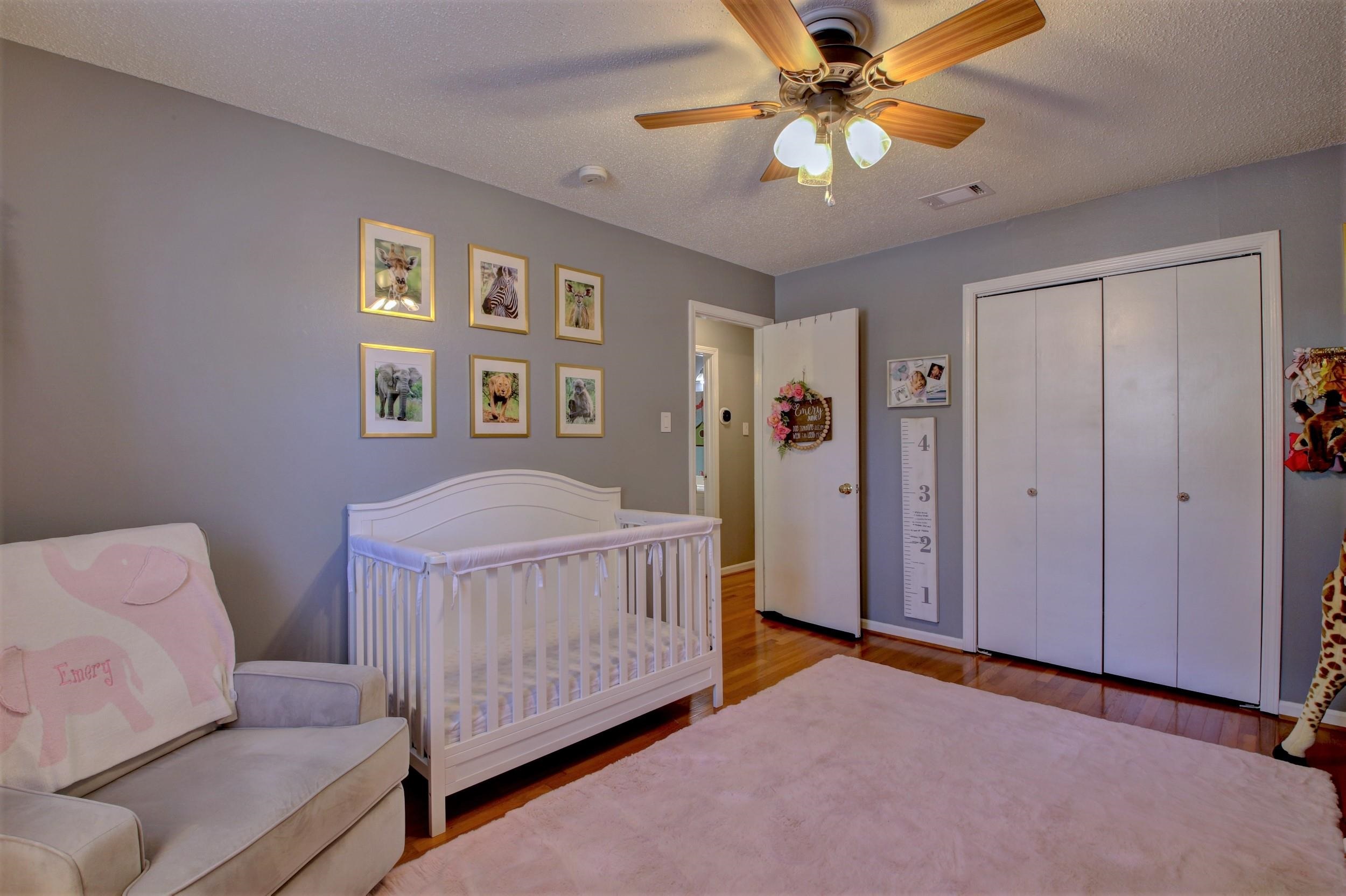 Furnished nursery with a white crib, pink rug, animal prints, and white closet doors.