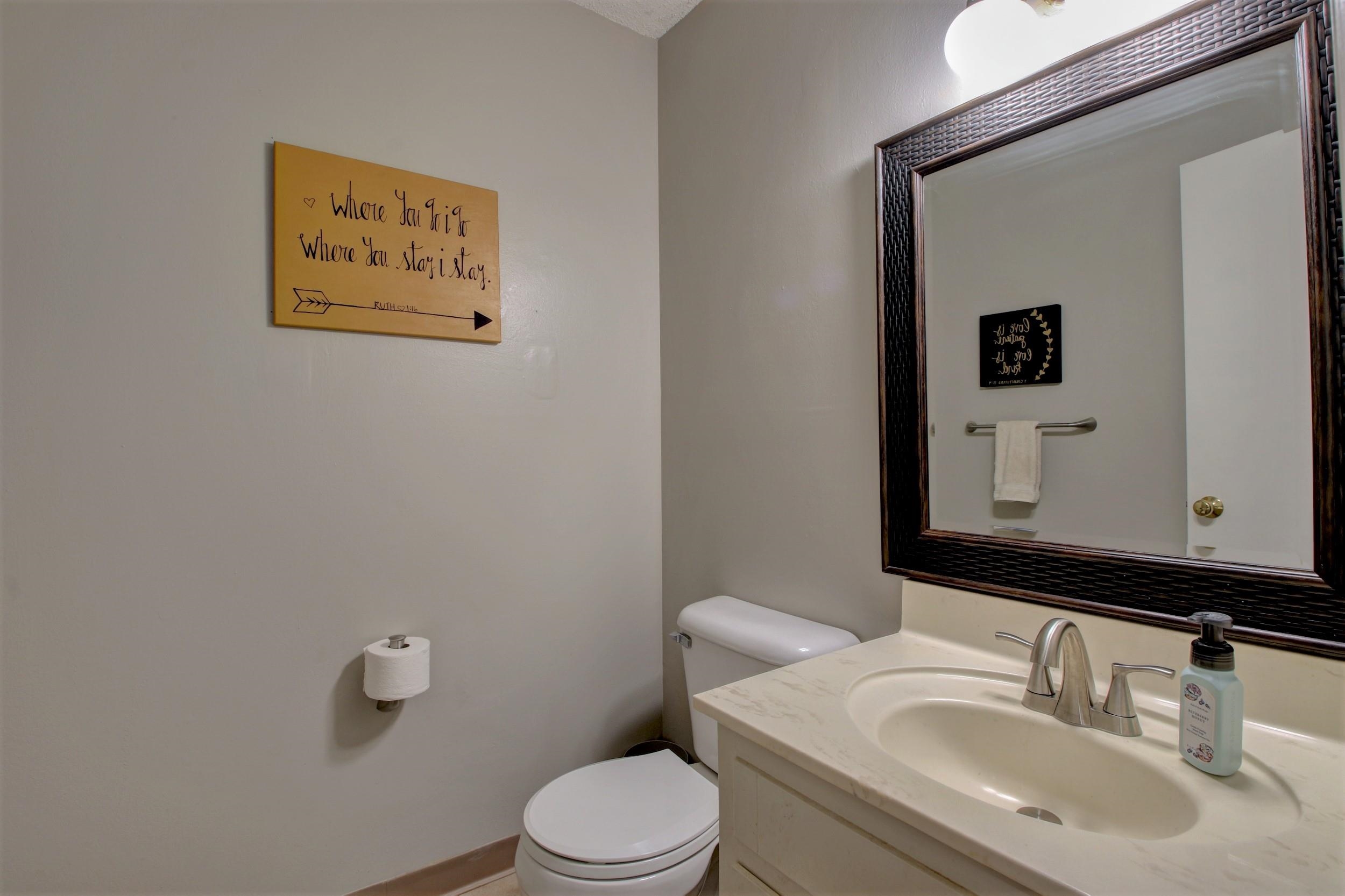 Bathroom with a cream vanity, oval sink, large framed mirror, and wooden quote sign.