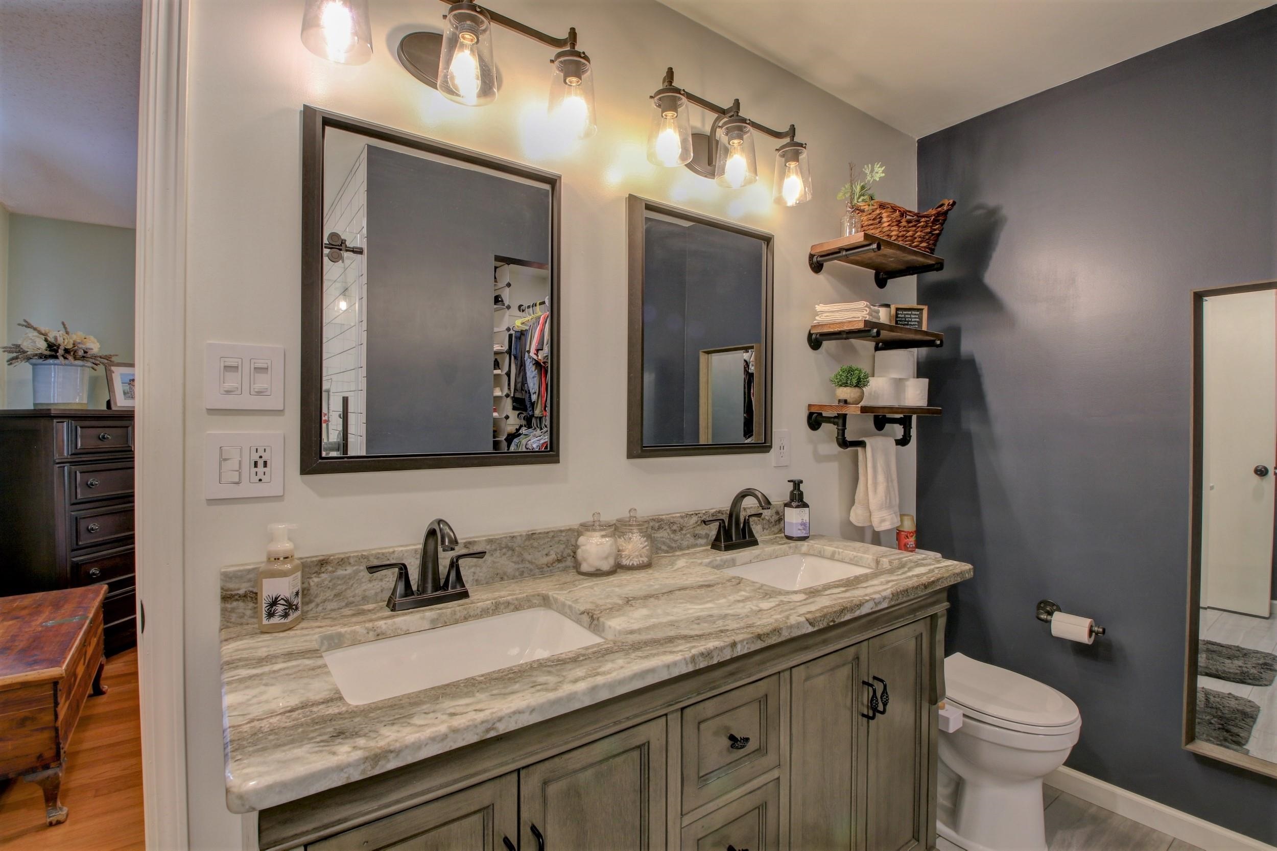 Bathroom with a double-sink stone vanity, framed mirrors, and dark gray accent wall.