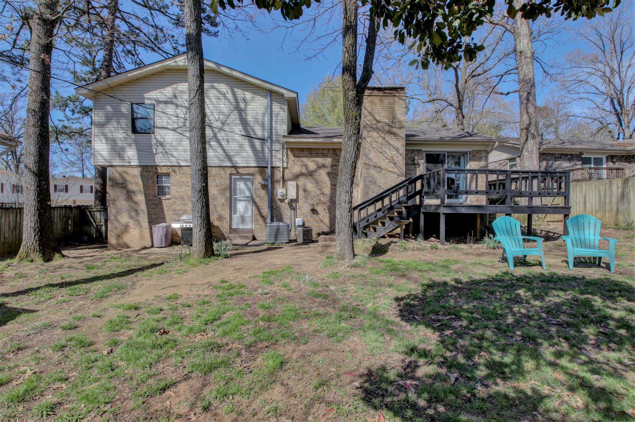 Rear of a two-story home with a raised deck, stairs, and two turquoise chairs in the backyard.