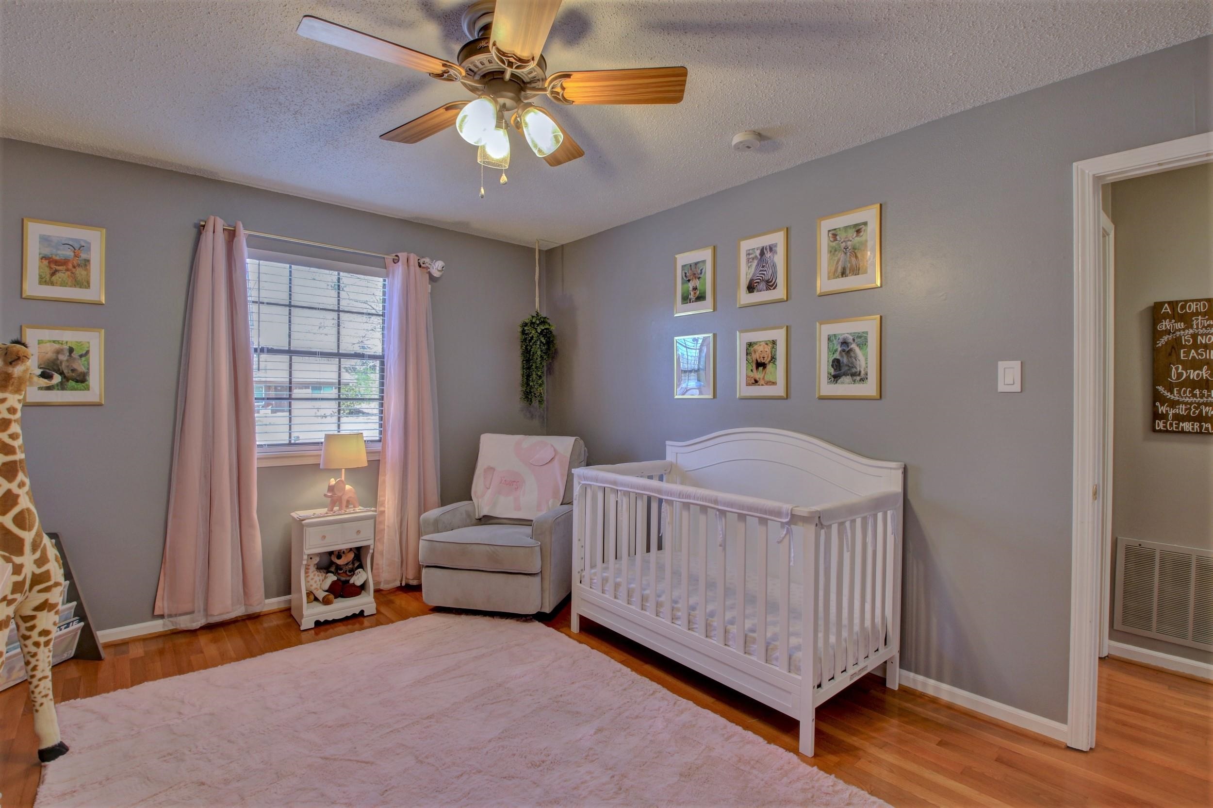 Nursery with a white crib, gray glider chair, pink curtains, and animal prints.