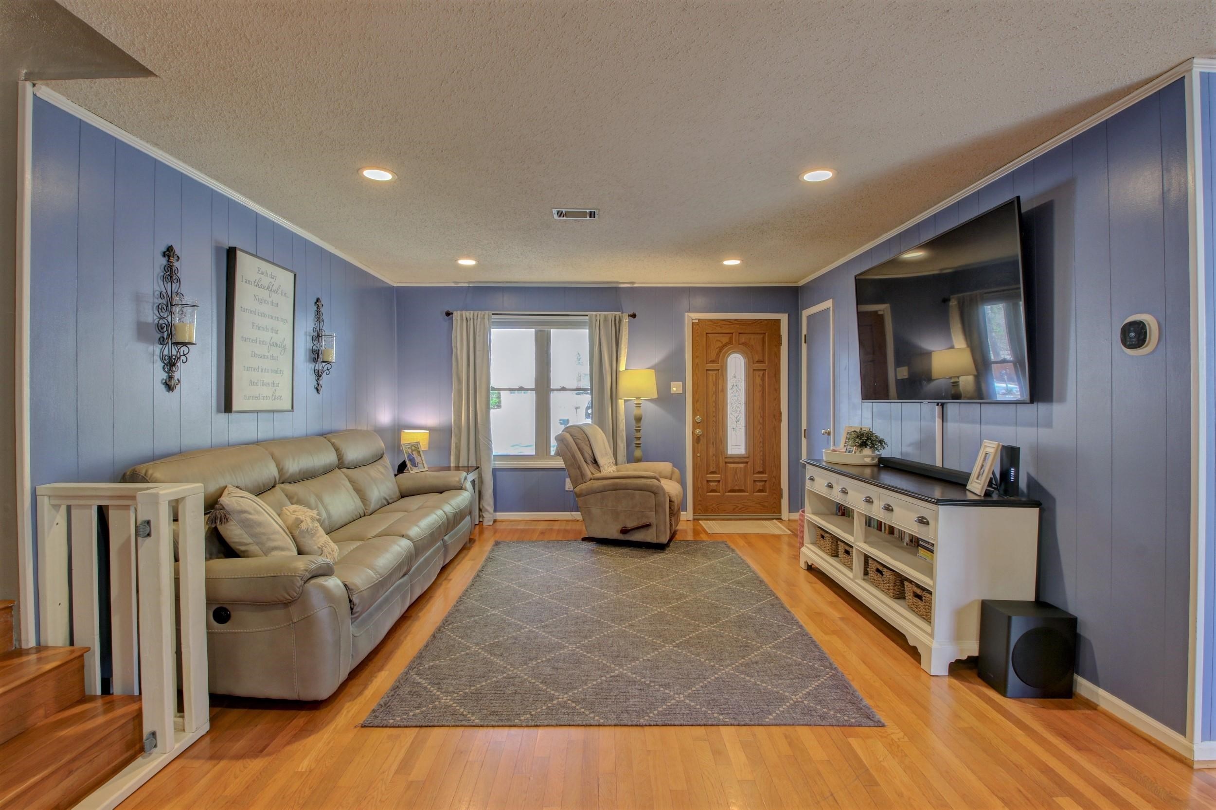 Furnished living room with blue paneled walls, leather sofa, recliner, and wall-mounted television.