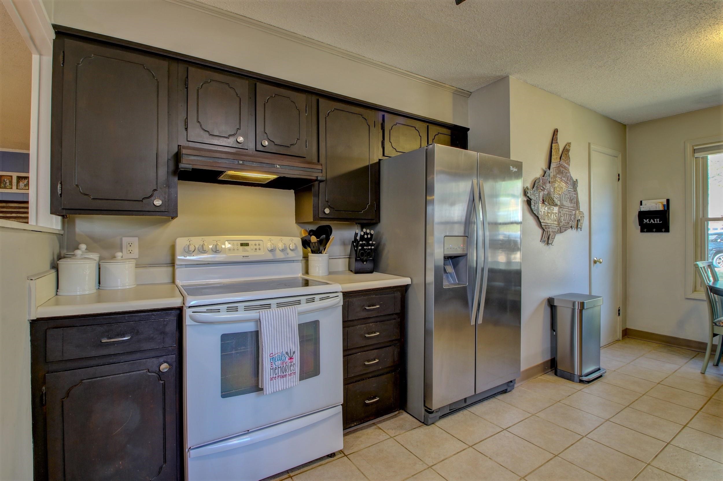 Kitchen with dark wood cabinets, white electric range, and stainless-steel refrigerator.