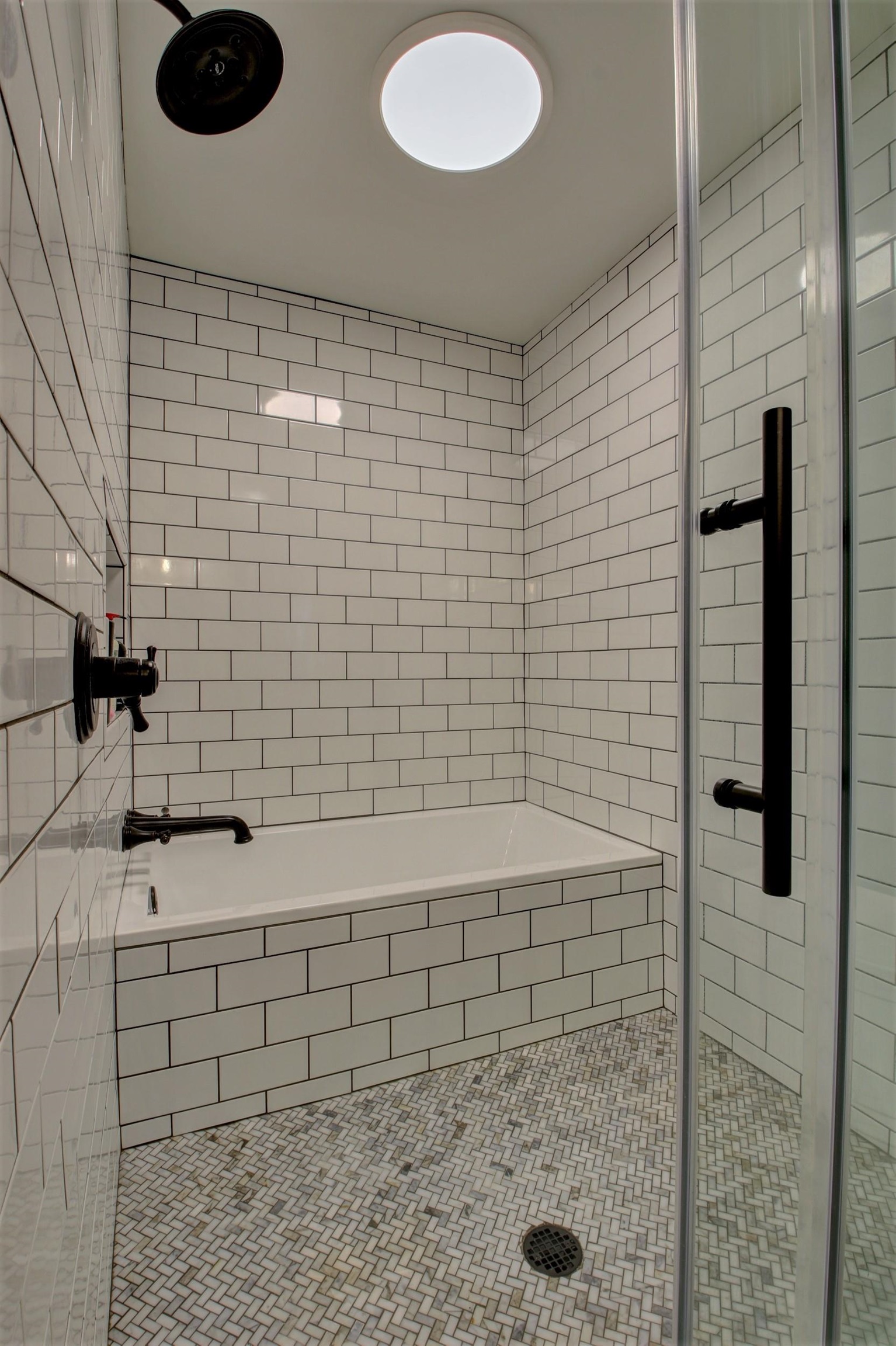 Tiled bathroom shower and bathtub with black fixtures and a mosaic floor.