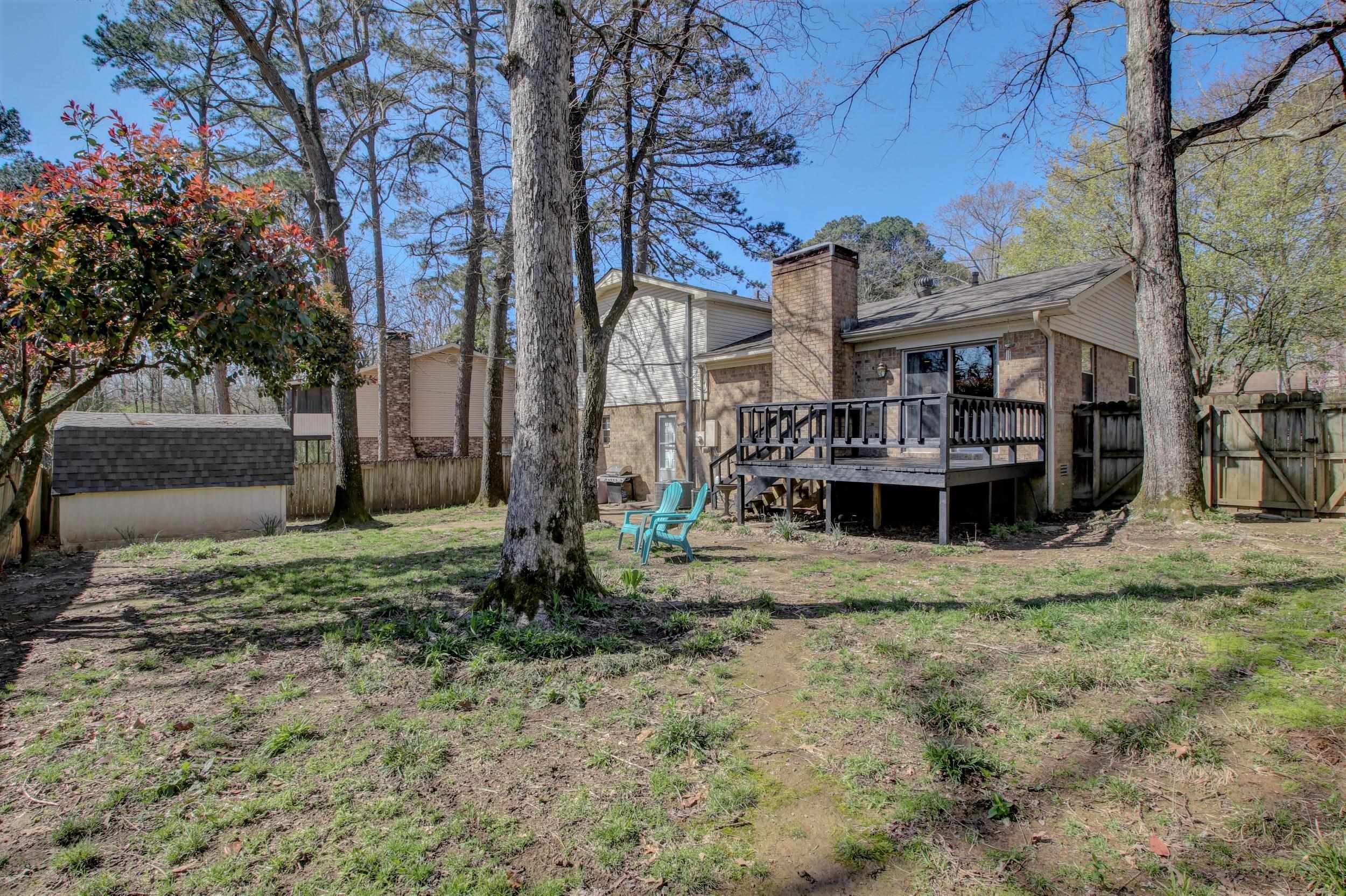 Home’s wooded backyard with a raised deck, brick chimney, shed, and turquoise chairs.