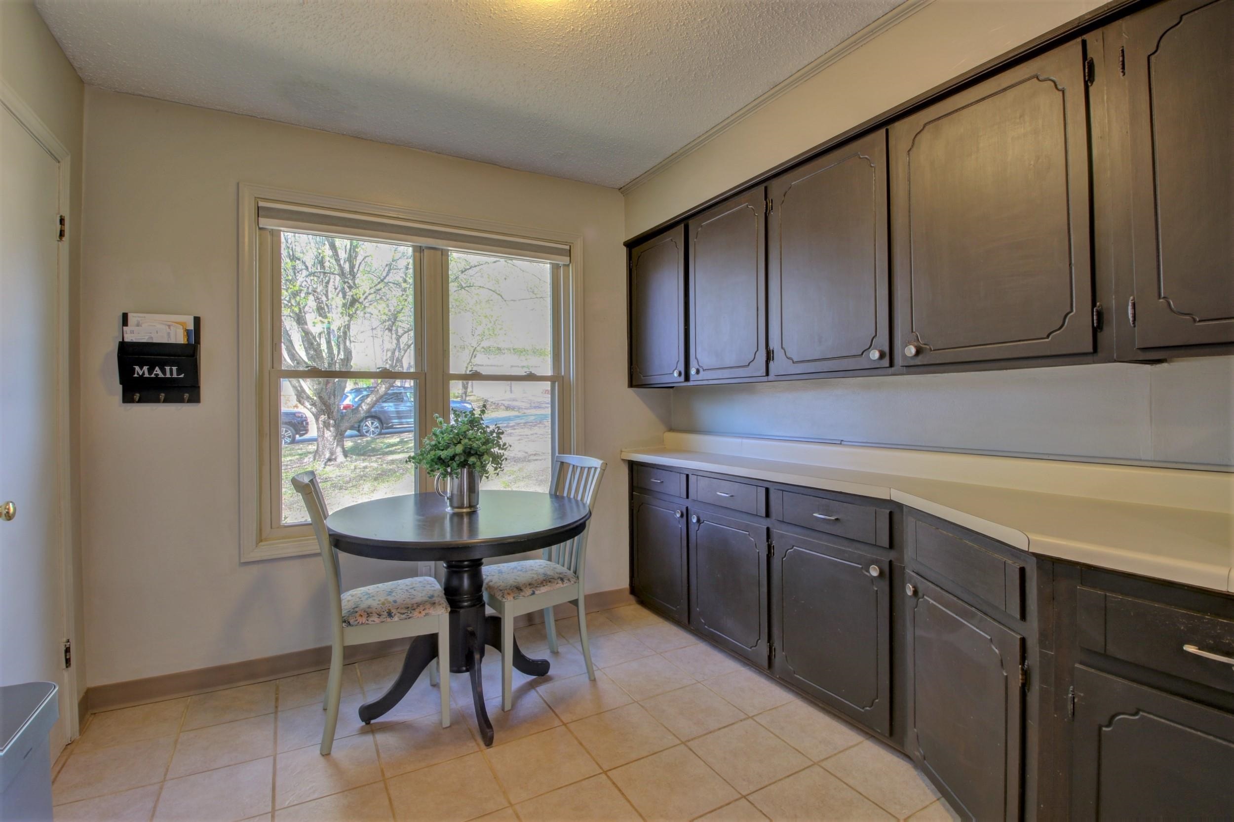 Kitchen with dark cabinets and a round breakfast table beside a large window.