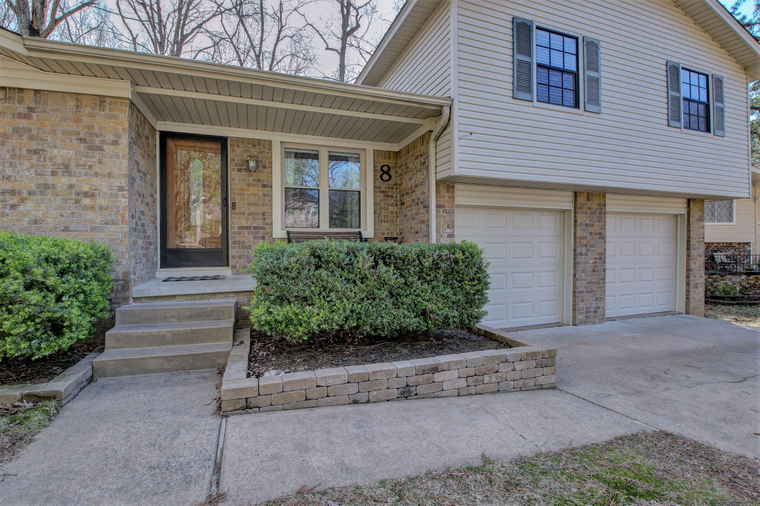 Two-story brick and beige-sided home with covered entry, front shrubs, and two garage doors.
