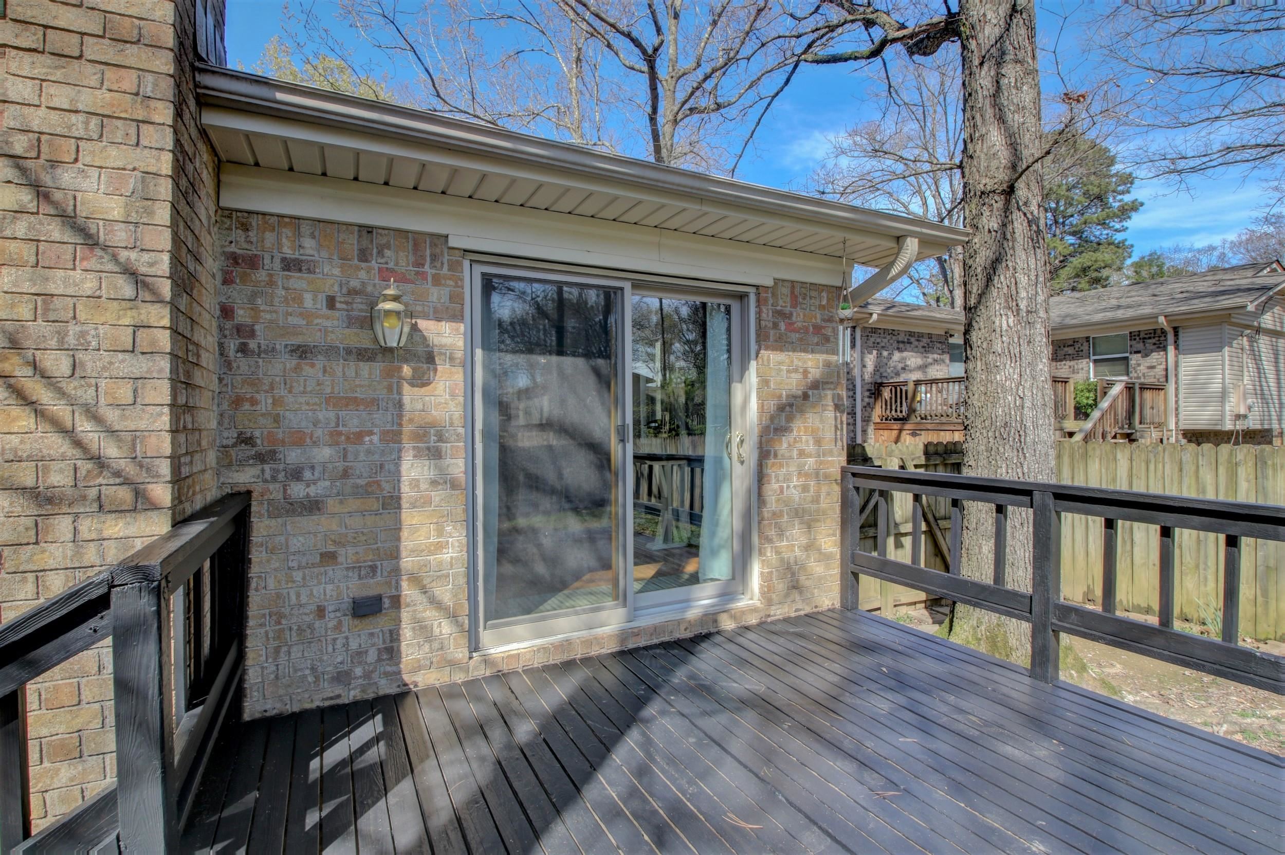 Wood deck beside a brick home, with black railings and a sliding glass door.