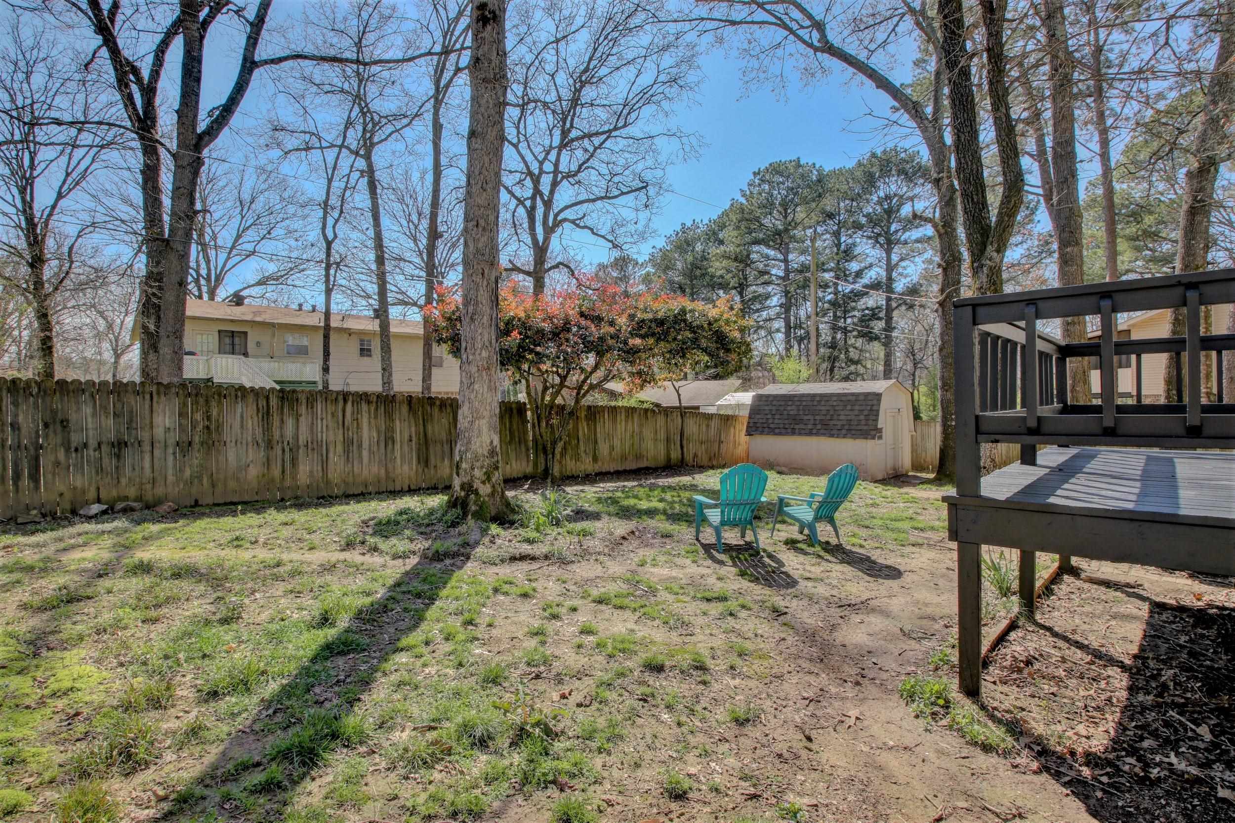 Fenced backyard with a raised deck, two turquoise chairs, and a storage shed beneath mature trees.