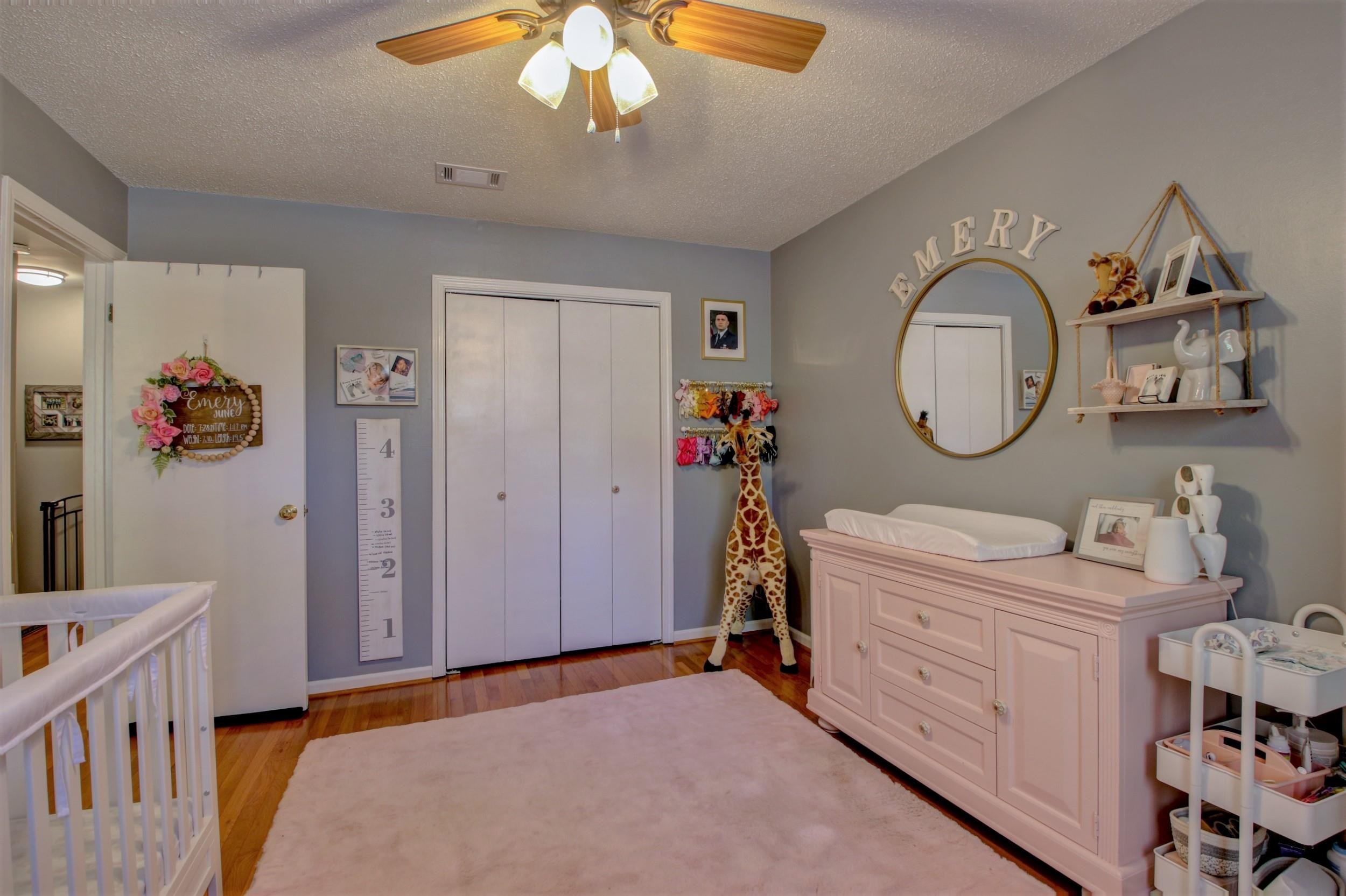 Nursery with a white crib, pink changing dresser, and giraffe decoration beside the closet.