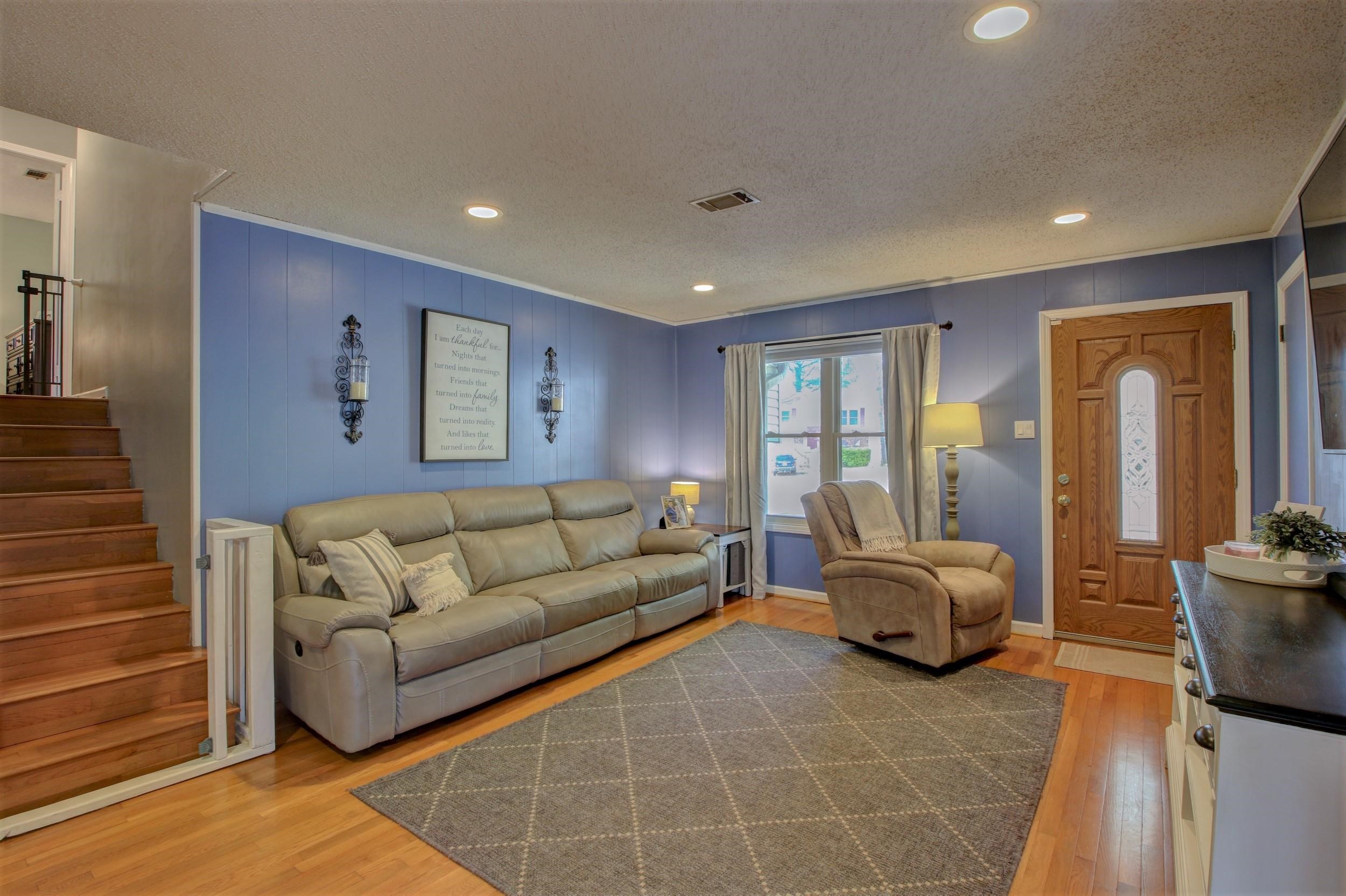 Living room with blue paneled walls, a leather sofa, recliner, hardwood floors, and a staircase.