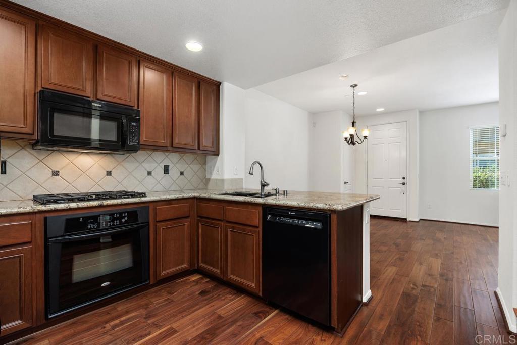 Kitchen with wood cabinets, granite counters, black appliances, and an open dining area.