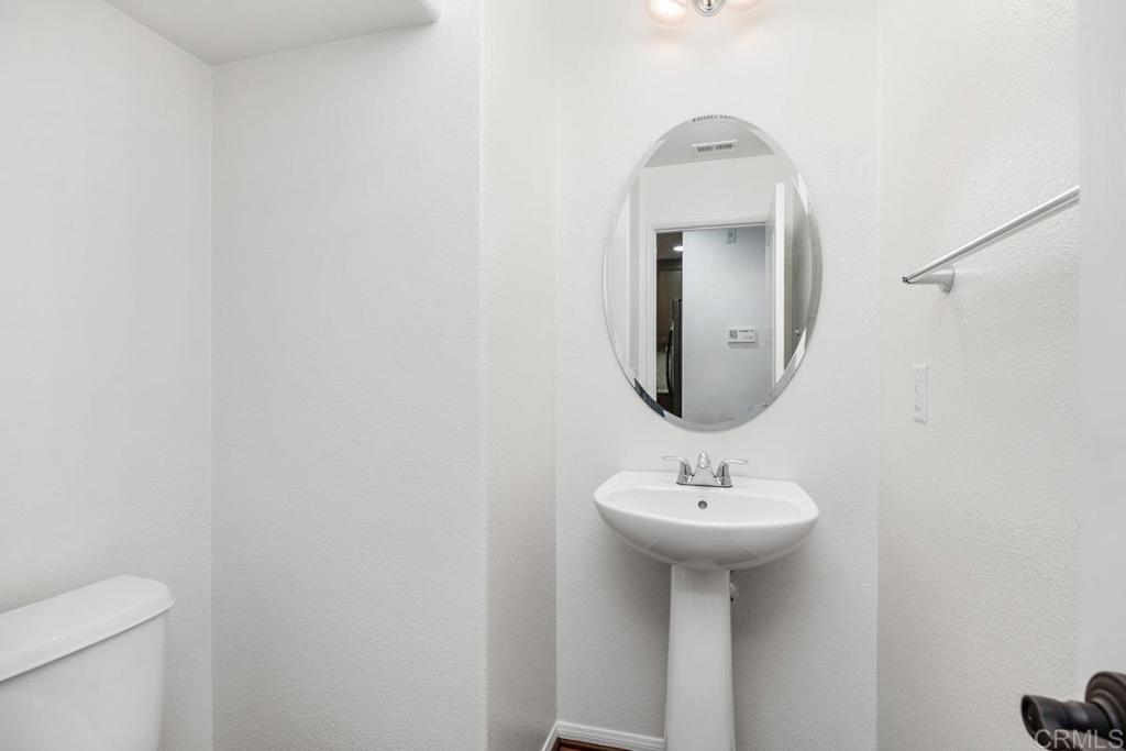 Bathroom with a white pedestal sink, oval mirror, and chrome towel bar.