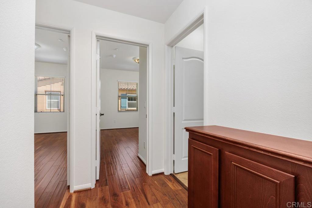 Hallway with wood floors and open doorways to two empty rooms, beside a reddish-brown cabinet.