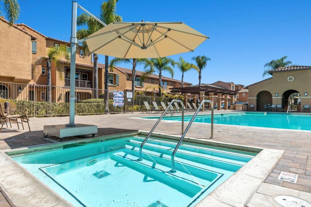 Community pool courtyard with a shallow spa, large umbrella, lounge chairs, and surrounding townhomes.