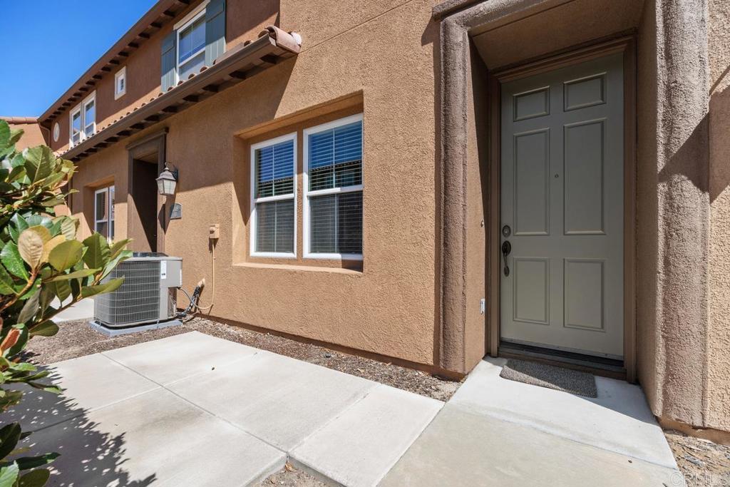 Tan stucco home with a recessed gray front door and concrete walkway.