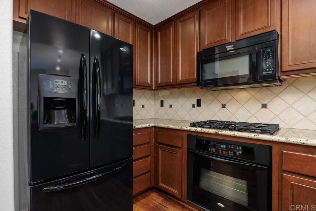 Kitchen with wood cabinetry, black appliances, a gas cooktop, and a cream tile backsplash.