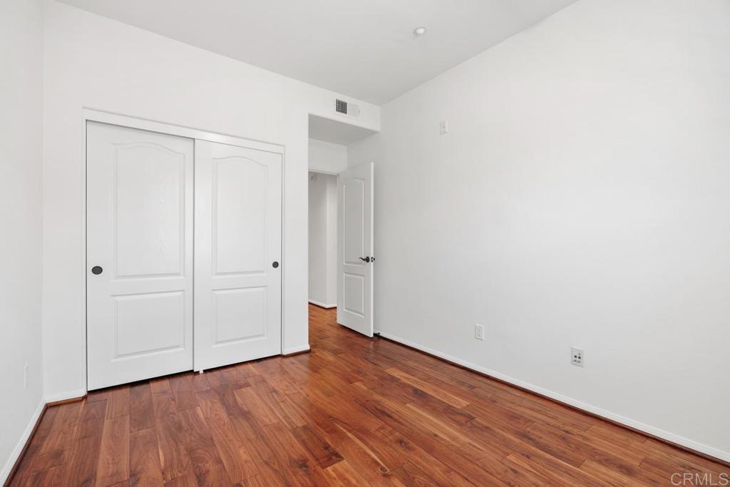 Empty bedroom with hardwood floors, double closet doors, and an open doorway.
