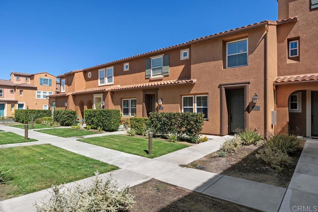 Attached stucco homes with tiled roofs and landscaped lawns beside a concrete walkway.