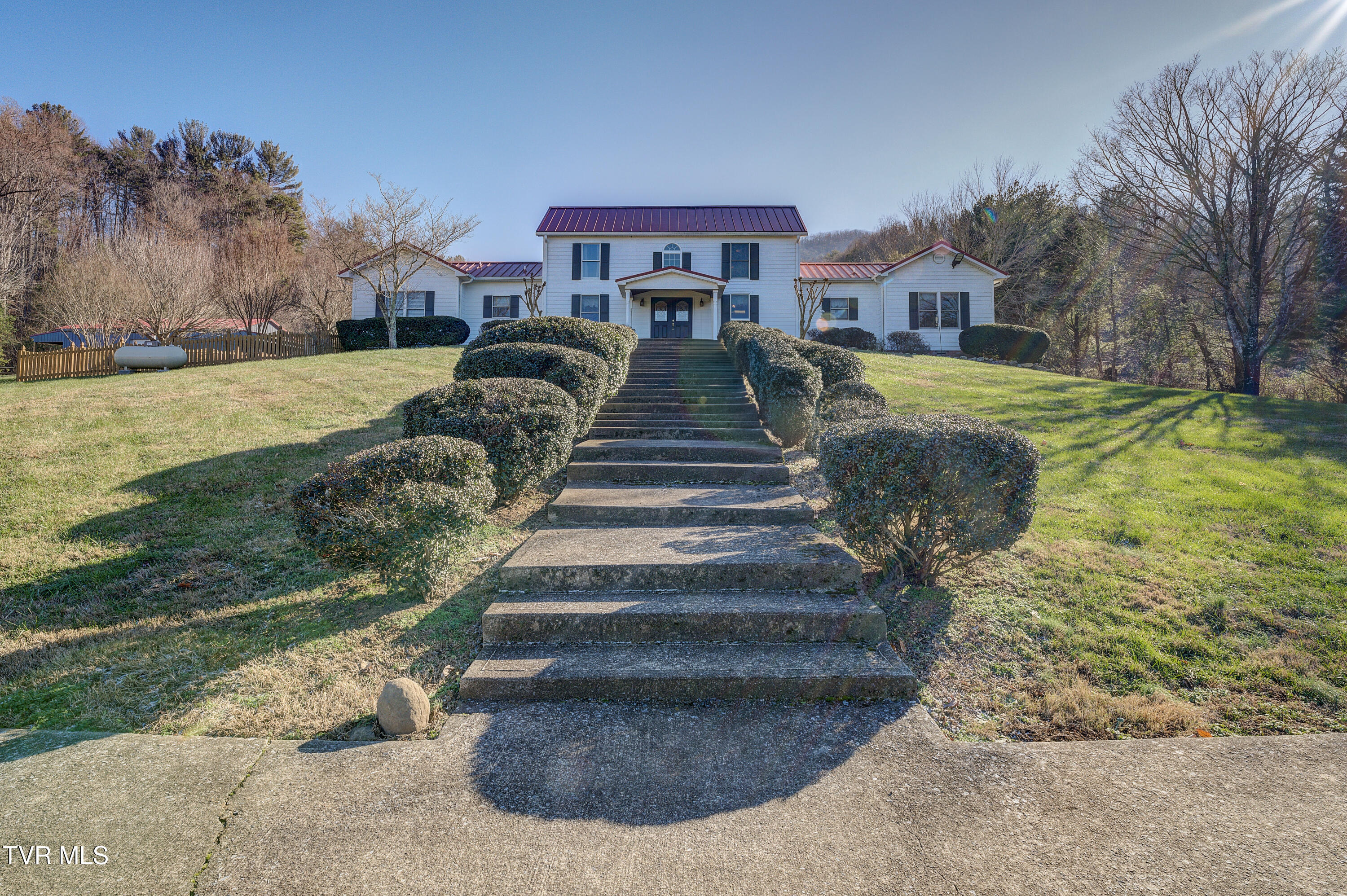 White two-story house with red metal roofs, reached by a long hedge-lined staircase.
