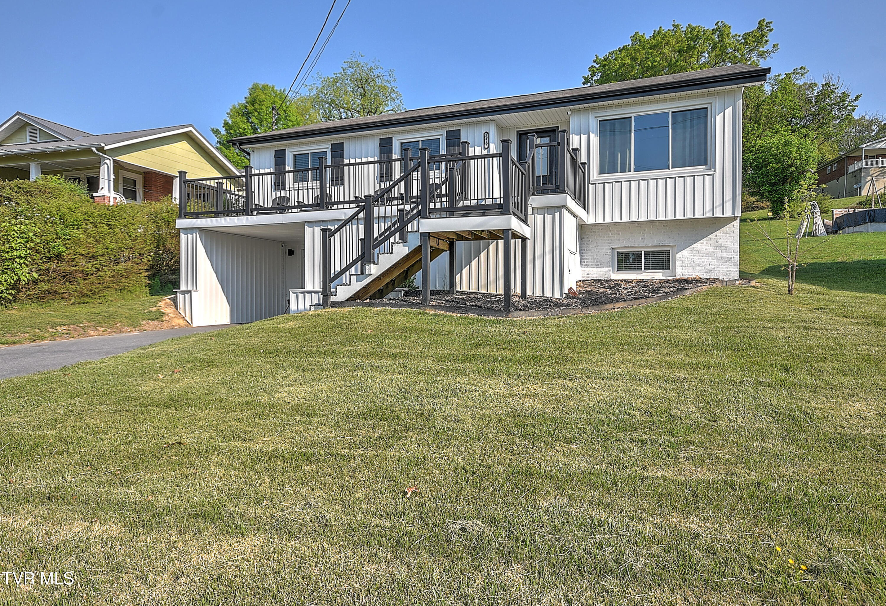 White-sided house with a raised deck and exterior stairs above a broad lawn.