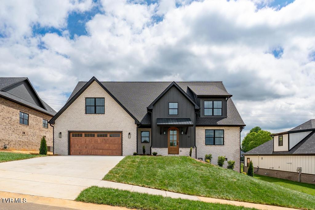Two-story brick and charcoal-sided home with a wood garage door and sloping front lawn.