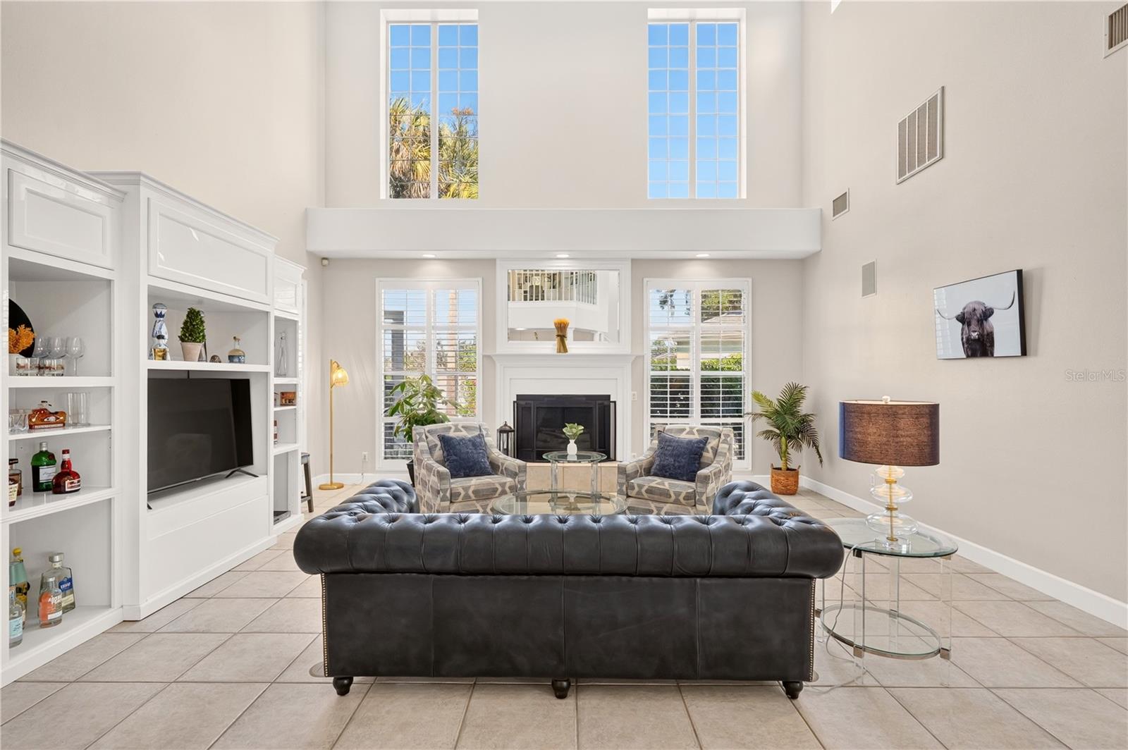 Living room with a double-height ceiling, tall windows, built-in shelving, and a fireplace.