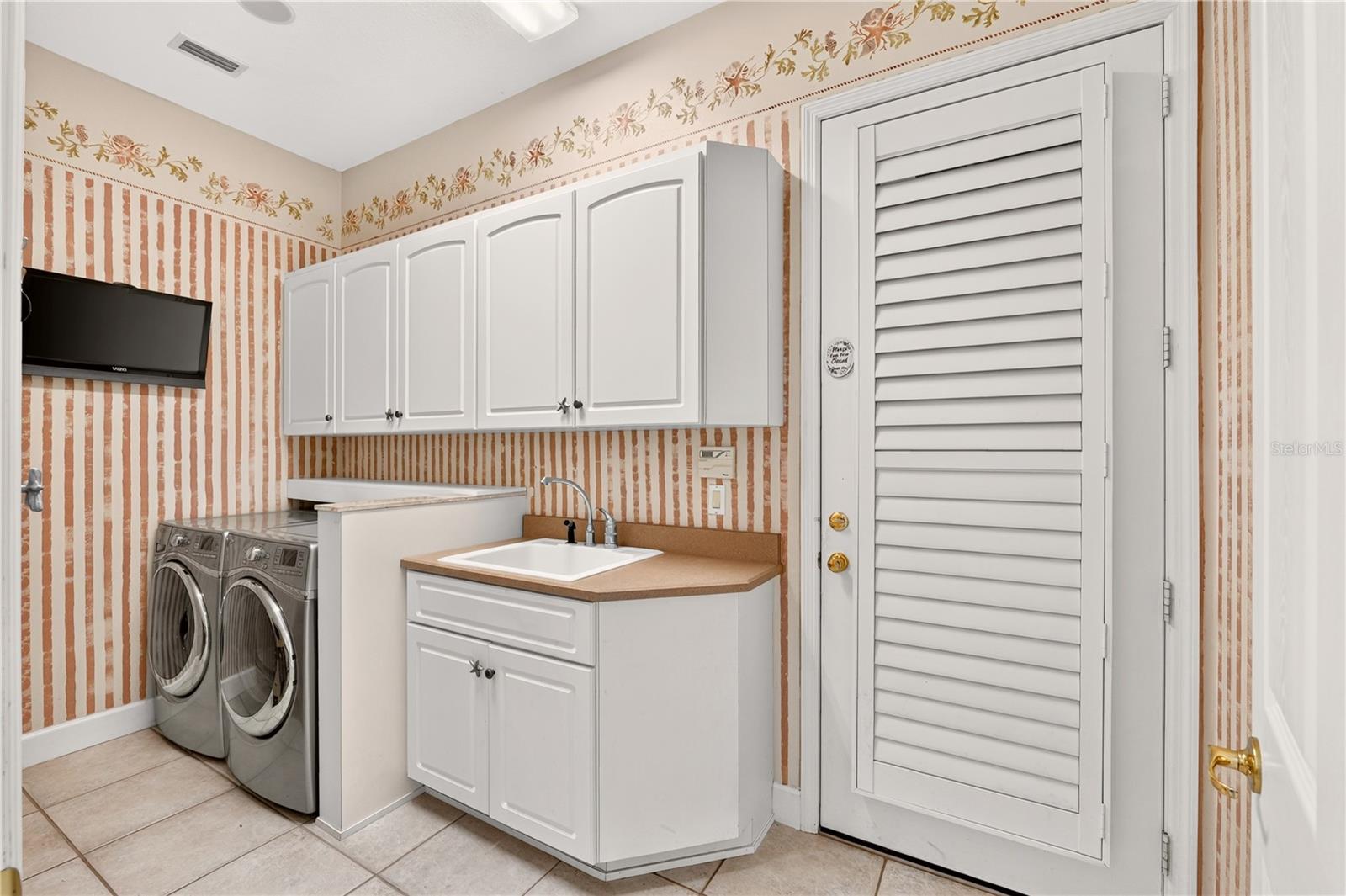 Laundry room with washer and dryer, white cabinets, utility sink, and louvered door.