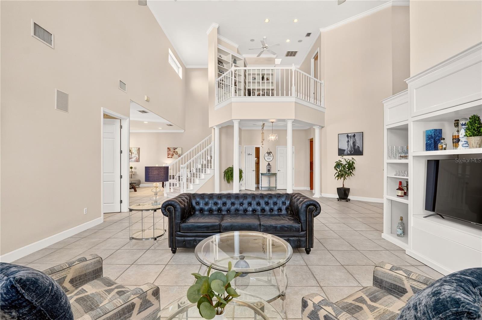 Furnished living room with a vaulted ceiling, upstairs balcony, staircase, and dark leather sofa.