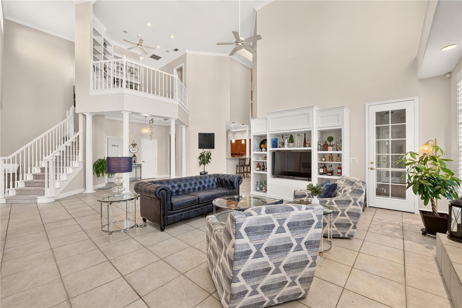 Furnished living room with vaulted ceiling, white staircase, built-in shelving, and blue seating.