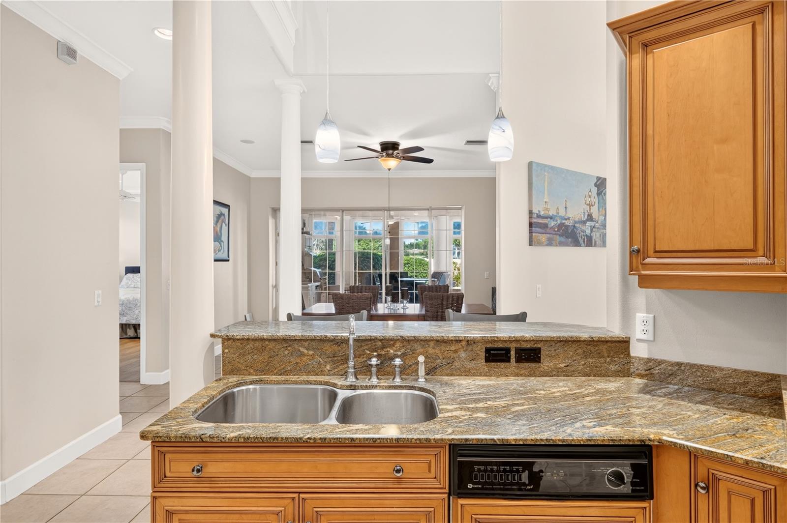 Kitchen with granite counters, wood cabinetry, a double sink, and dining area beyond.