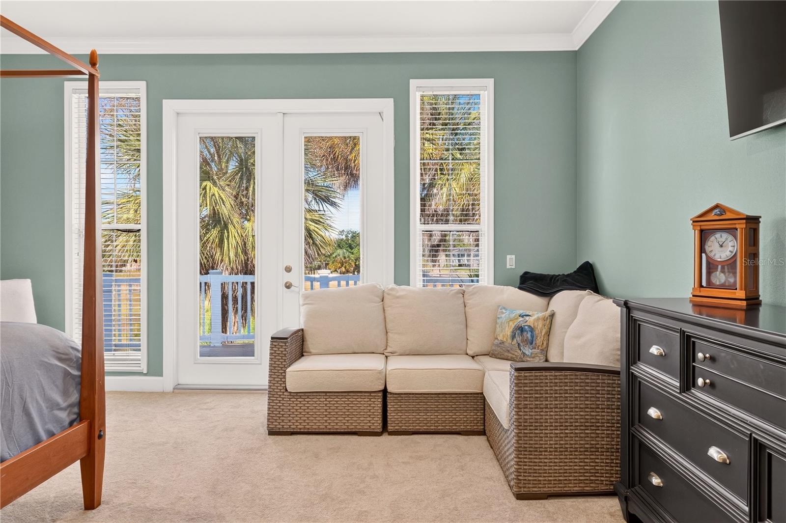 Furnished bedroom with a beige sectional sofa beside a glass door overlooking a pool and palm trees.