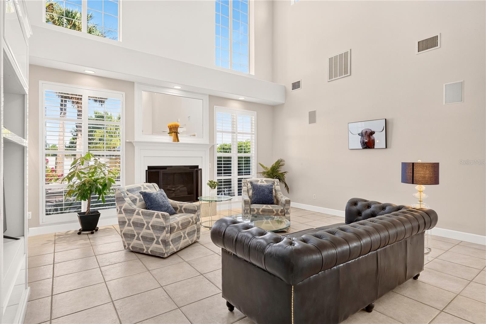 Living room with a fireplace, vaulted ceiling, plantation shutters, and dark leather sofa.