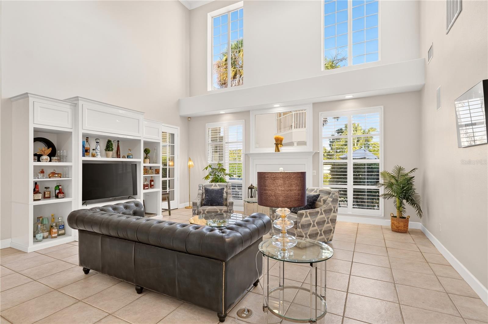 Double-height living room with a dark leather sectional, fireplace, and white built-in shelving.