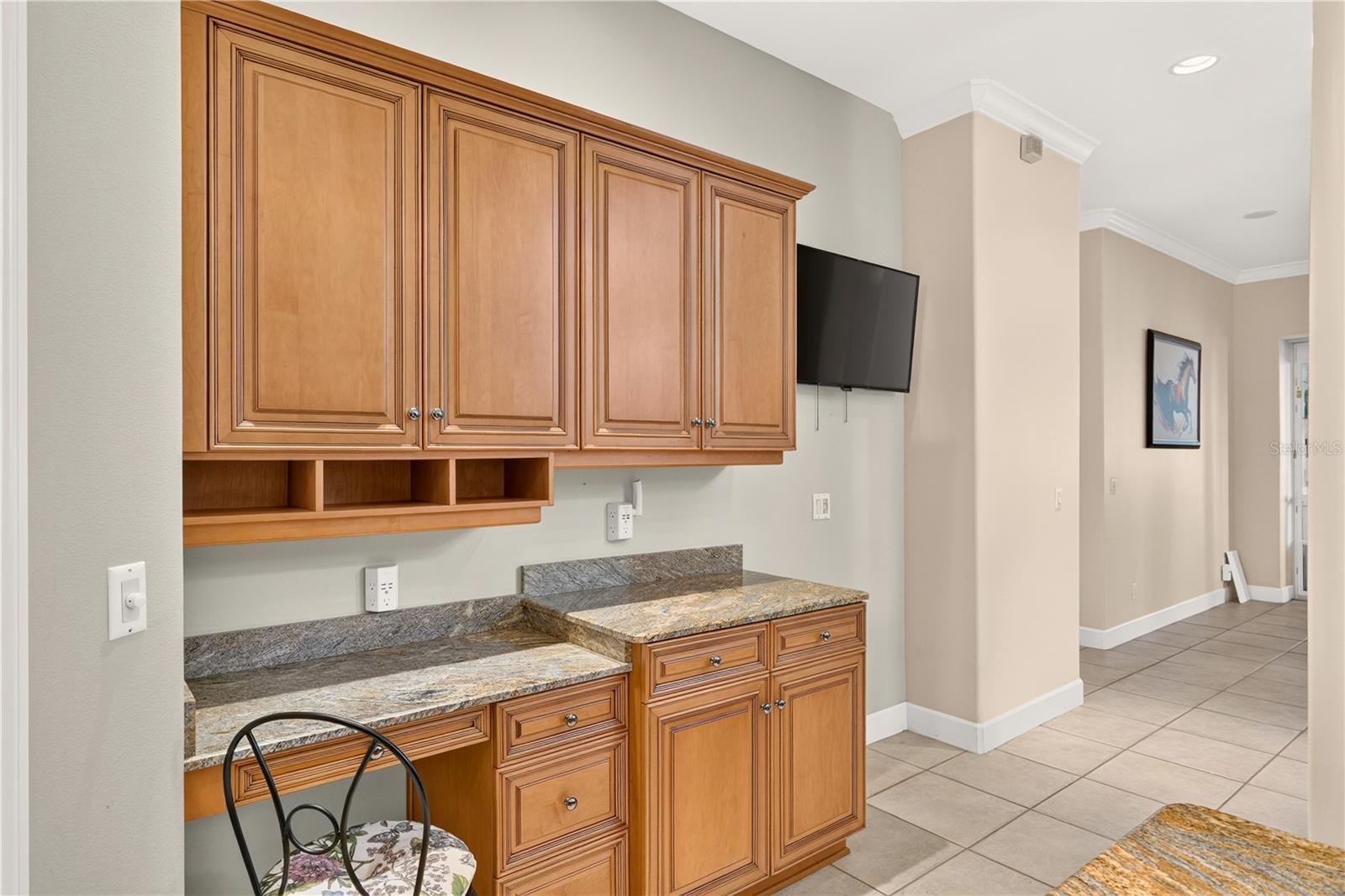 Built-in office cabinetry with granite counters, a desk nook, and wall-mounted television.