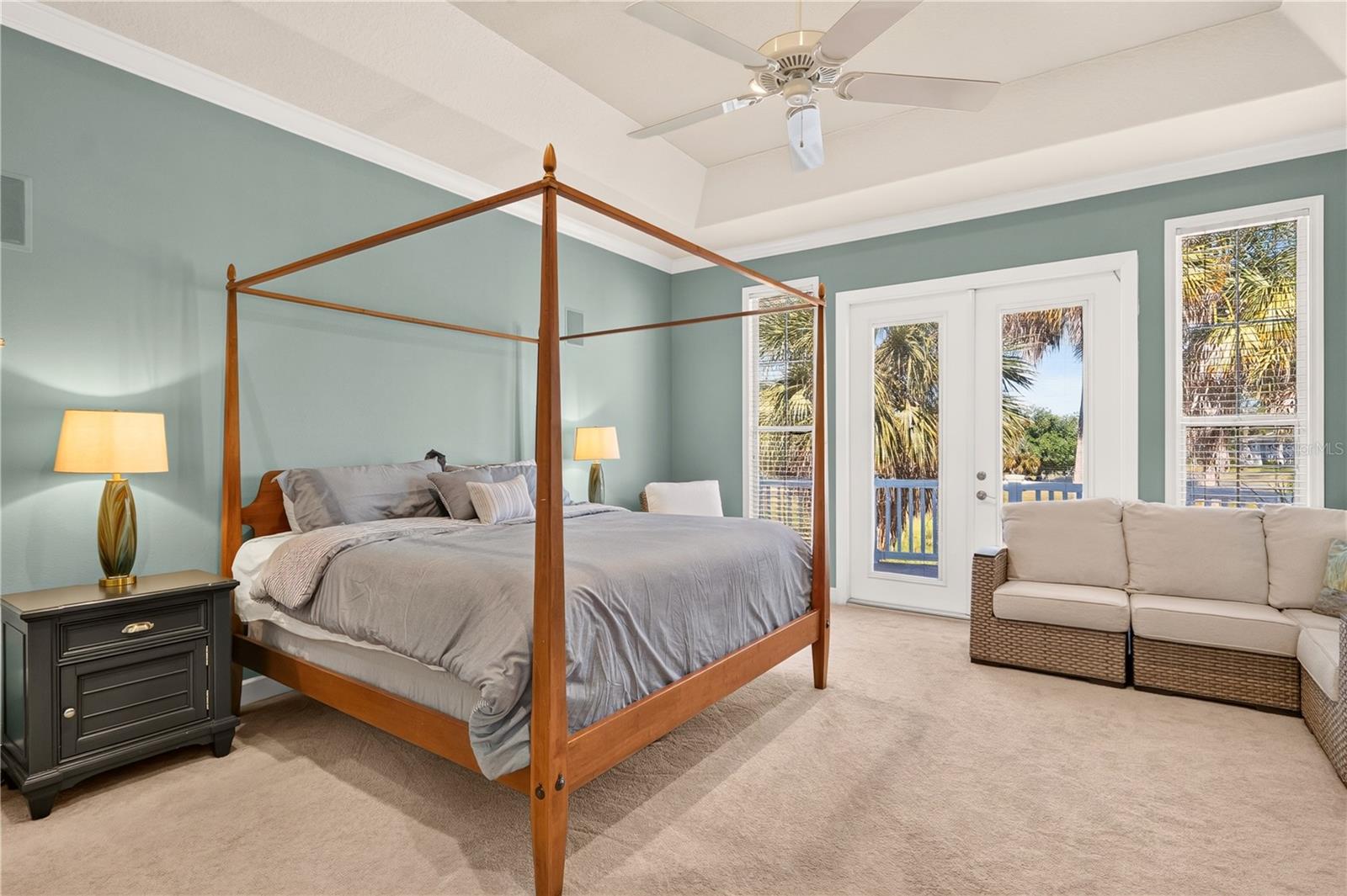 Furnished bedroom with a four-poster bed, ceiling fan, and glass doors overlooking water and palm trees.