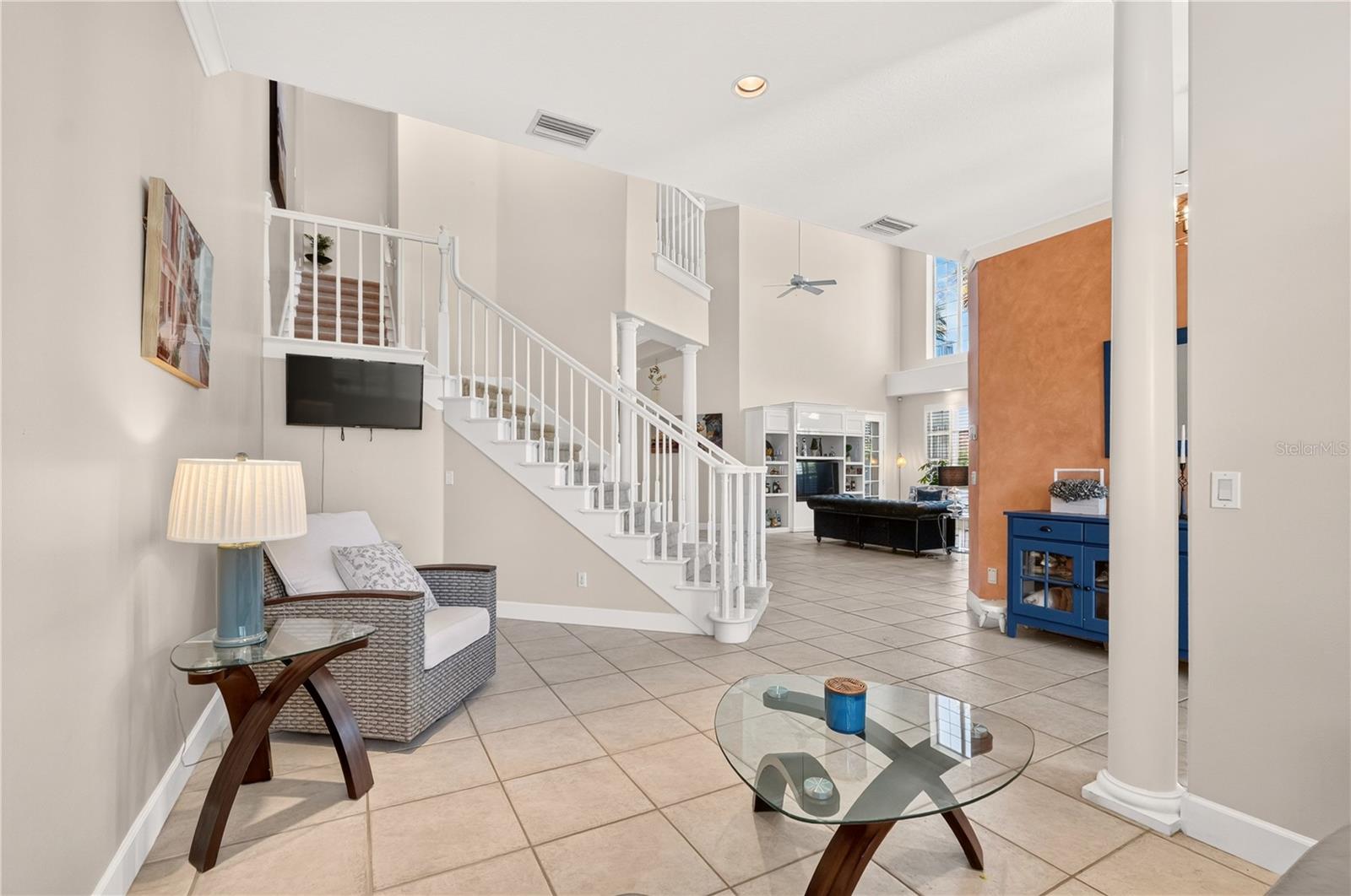 Two-story living room with a white staircase, tiled floors, and an orange accent wall.