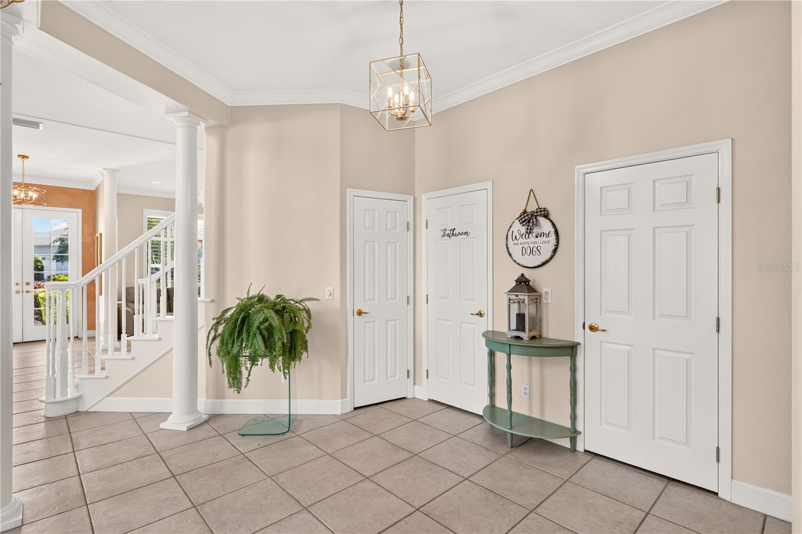 Tiled entry foyer with a white staircase, three paneled doors, and a green console table.