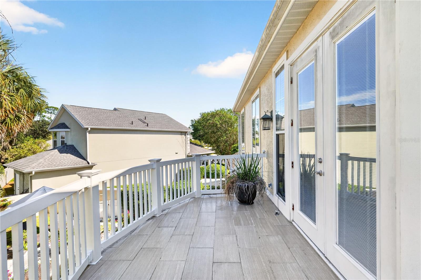 Tiled upper-level deck with white railings, tall glass doors, and a potted plant.