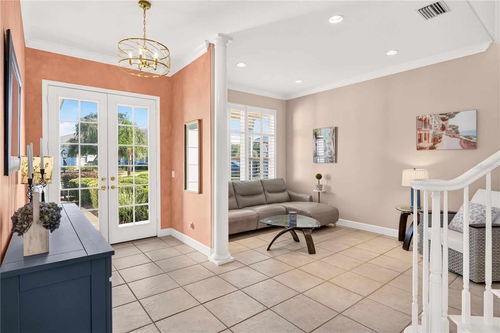 Living room with French doors, gray sectional sofa, tiled floors, and a white staircase railing.