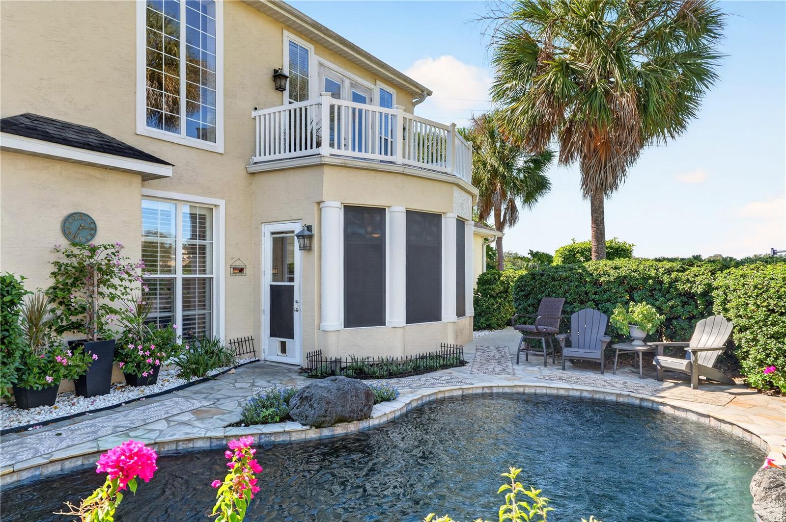 Cream stucco home with a white-railed balcony, screened patio, and curved pool.