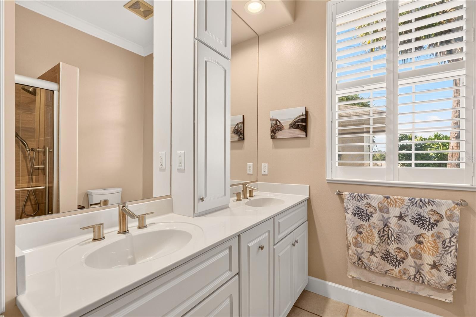 Bathroom with a white double-sink vanity, mirrored cabinet, and plantation-shuttered window.