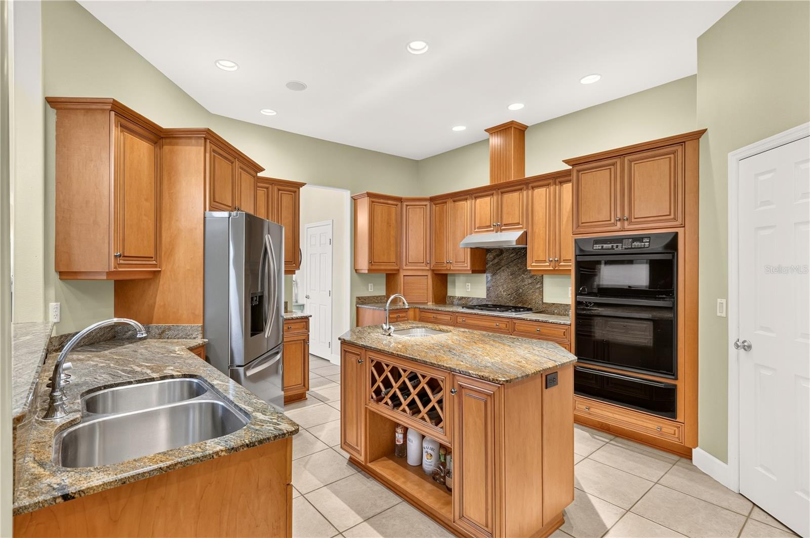 Kitchen with a granite island, honey-toned cabinetry, double sink, and built-in double ovens.
