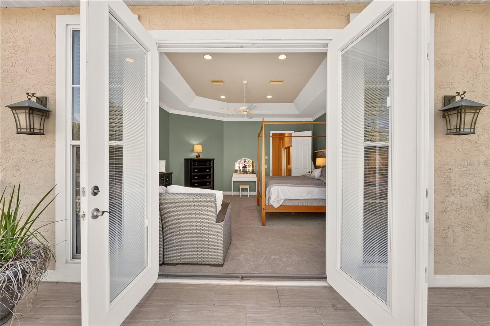 Furnished bedroom with green walls and tray ceiling, viewed through open French doors.