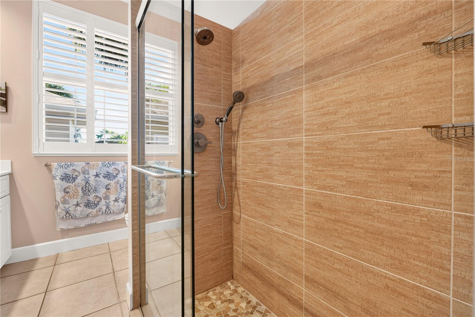 Bathroom shower with tan tile walls, glass enclosure, and pebble-tile floor.