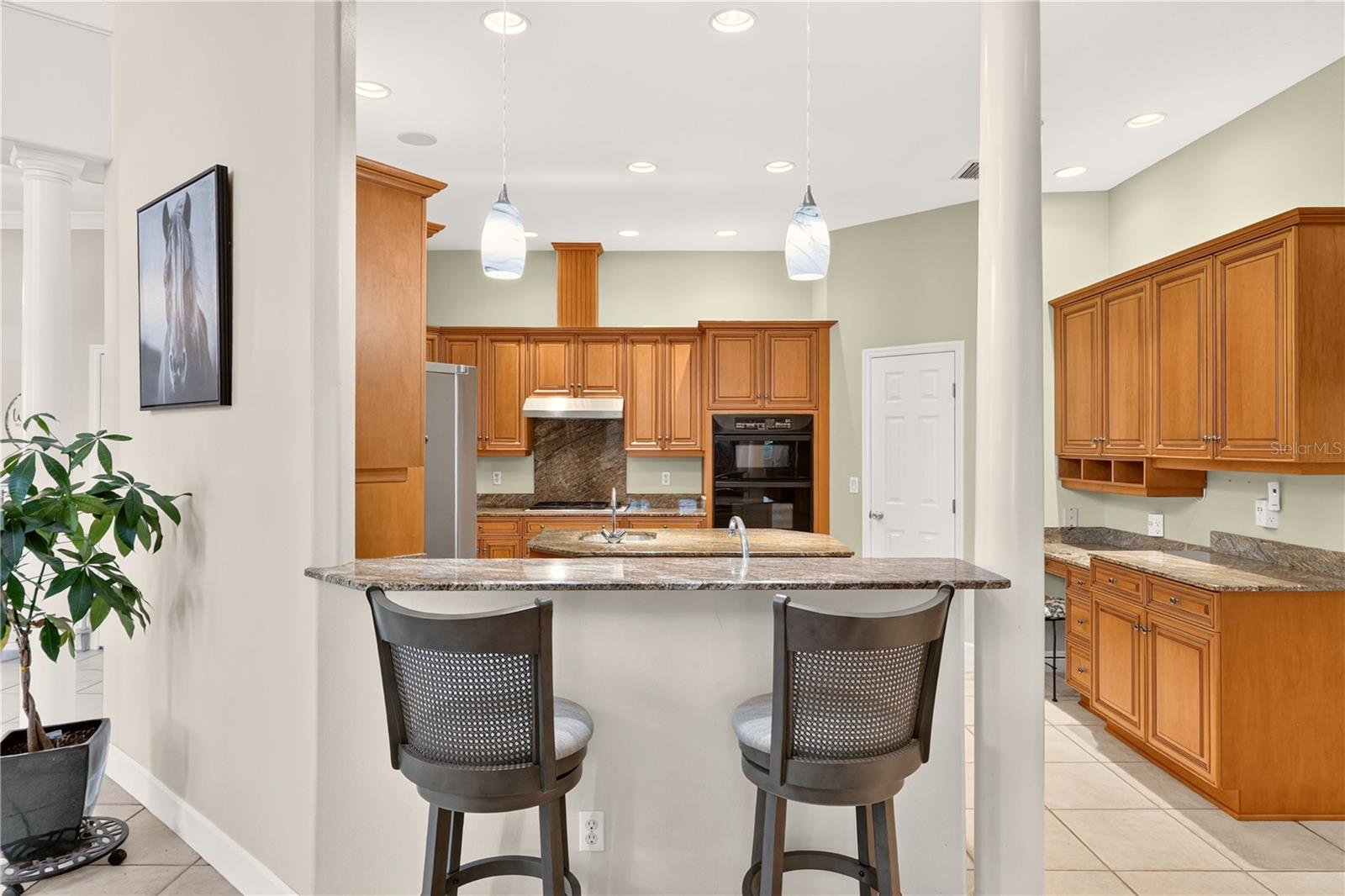 Kitchen with warm wood cabinetry, granite island, stainless steel appliances, and two bar stools.