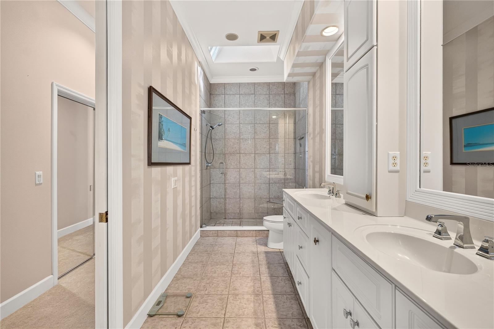 Bathroom with a double-sink vanity and glass-enclosed tiled shower.