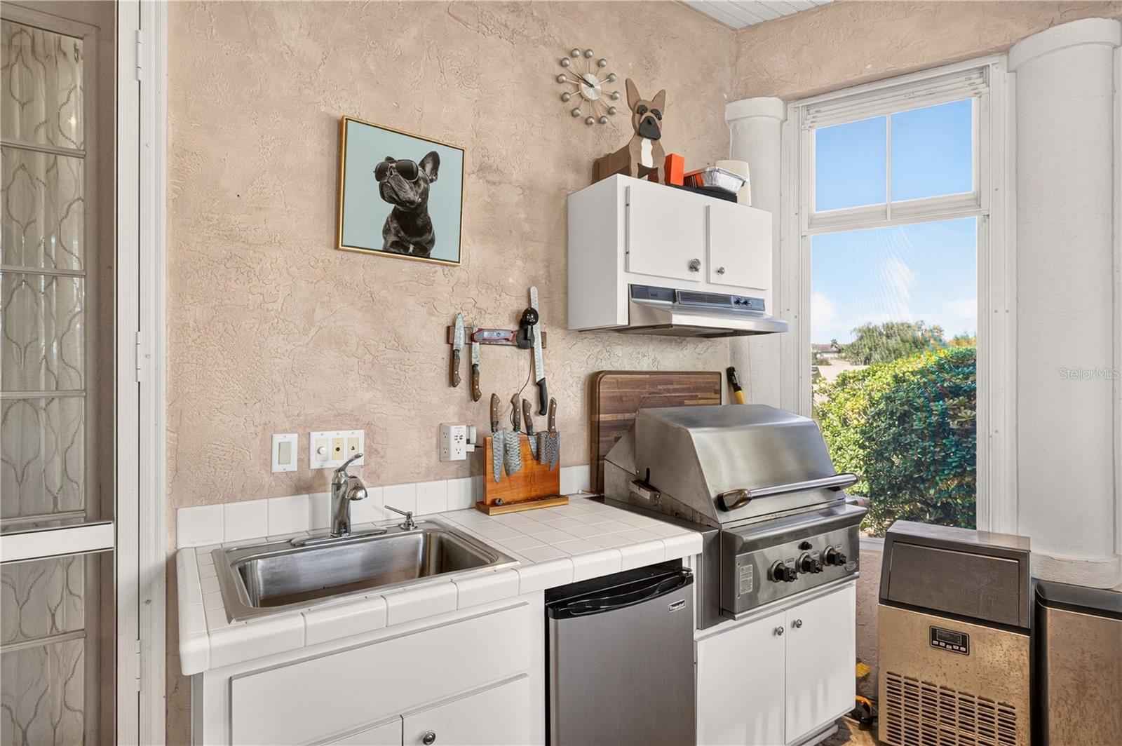 Kitchen with tiled counter, sink, built-in grill, and a large window overlooking greenery.
