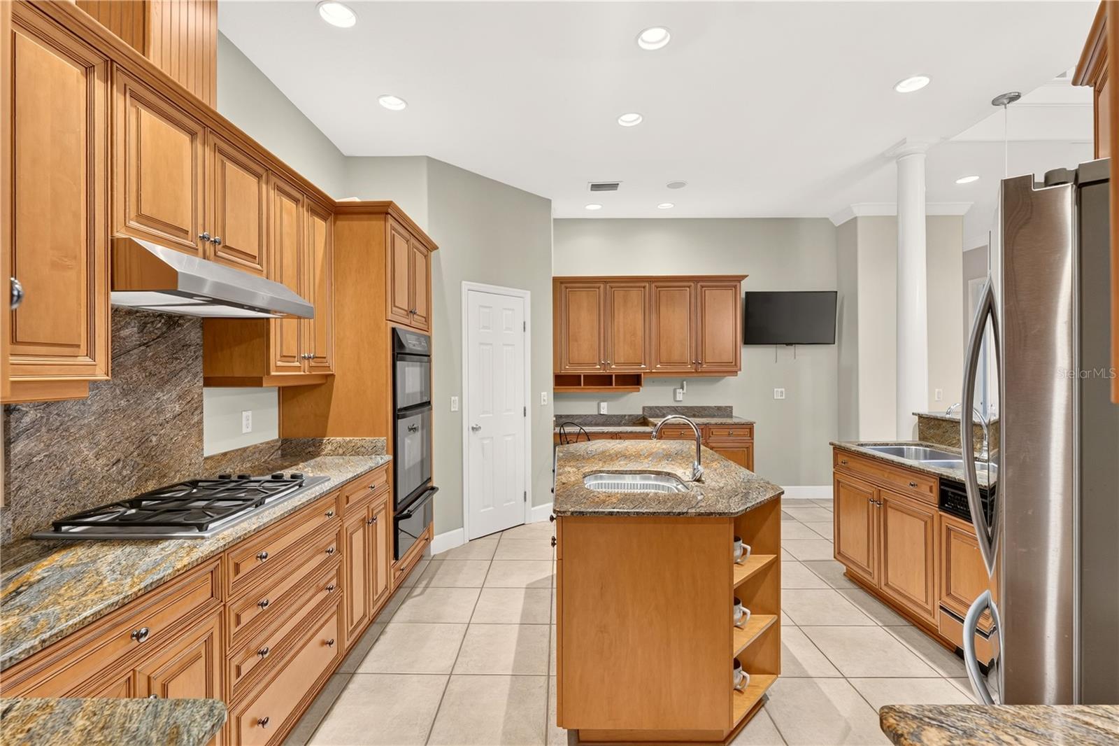 Kitchen with warm wood cabinetry, stone counters, a central sink island, and stainless steel appliances.
