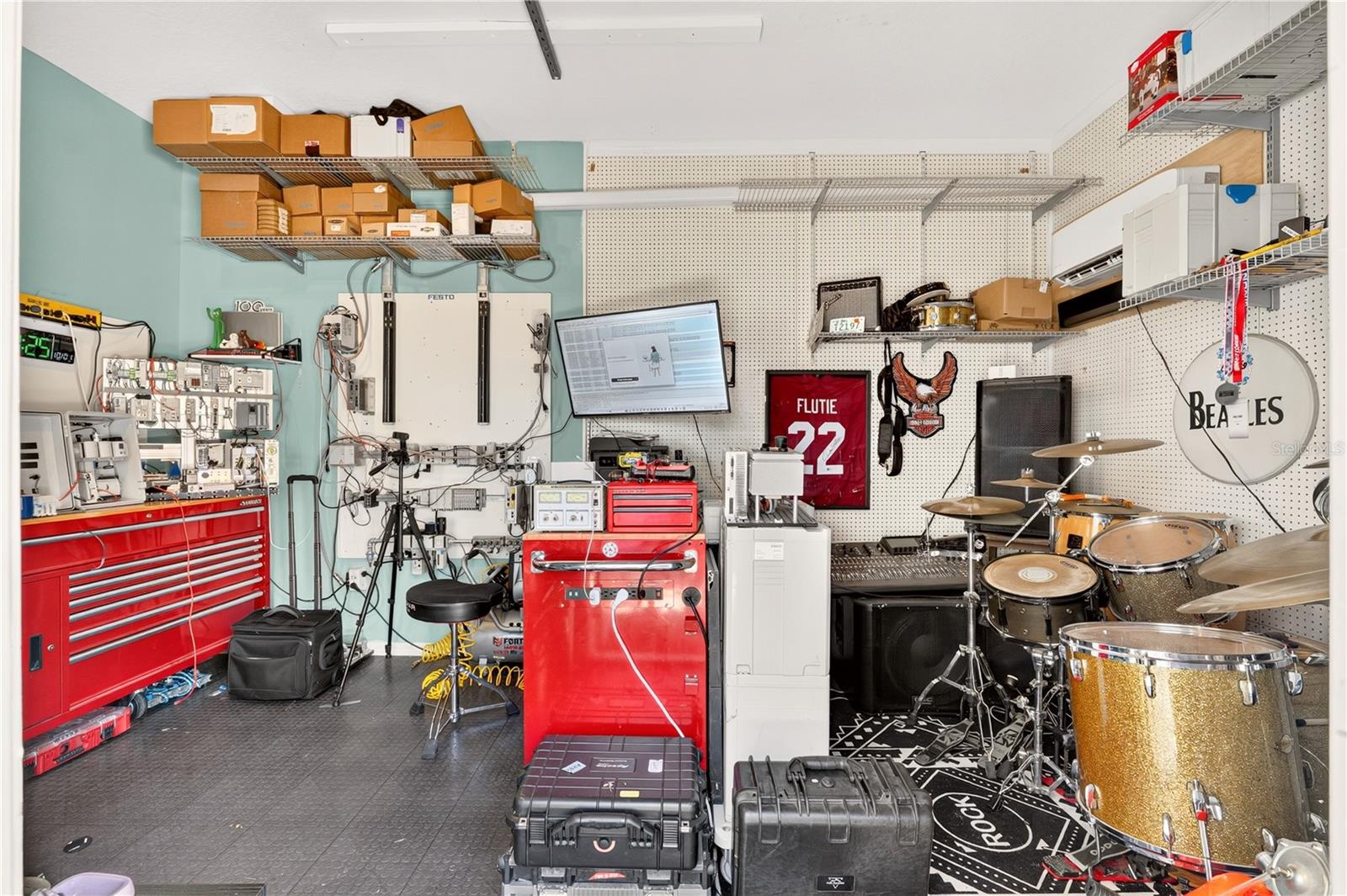 Garage workshop and music room with red tool chests, a drum kit, and Beatles wall sign.